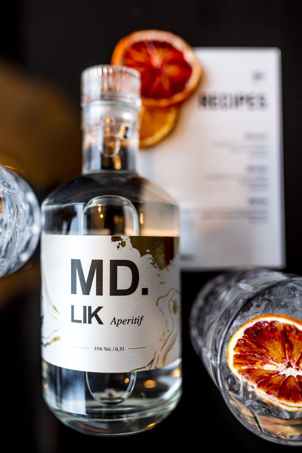 Flasche MD.LIK Aperitif mit getrockneten Orangenscheiben und Gläsern