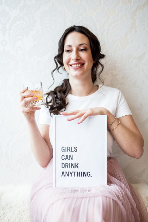 Frau hält ein Glas und ein Schild mit der Aufschrift „GIRLS CAN DRINK ANYTHING.“