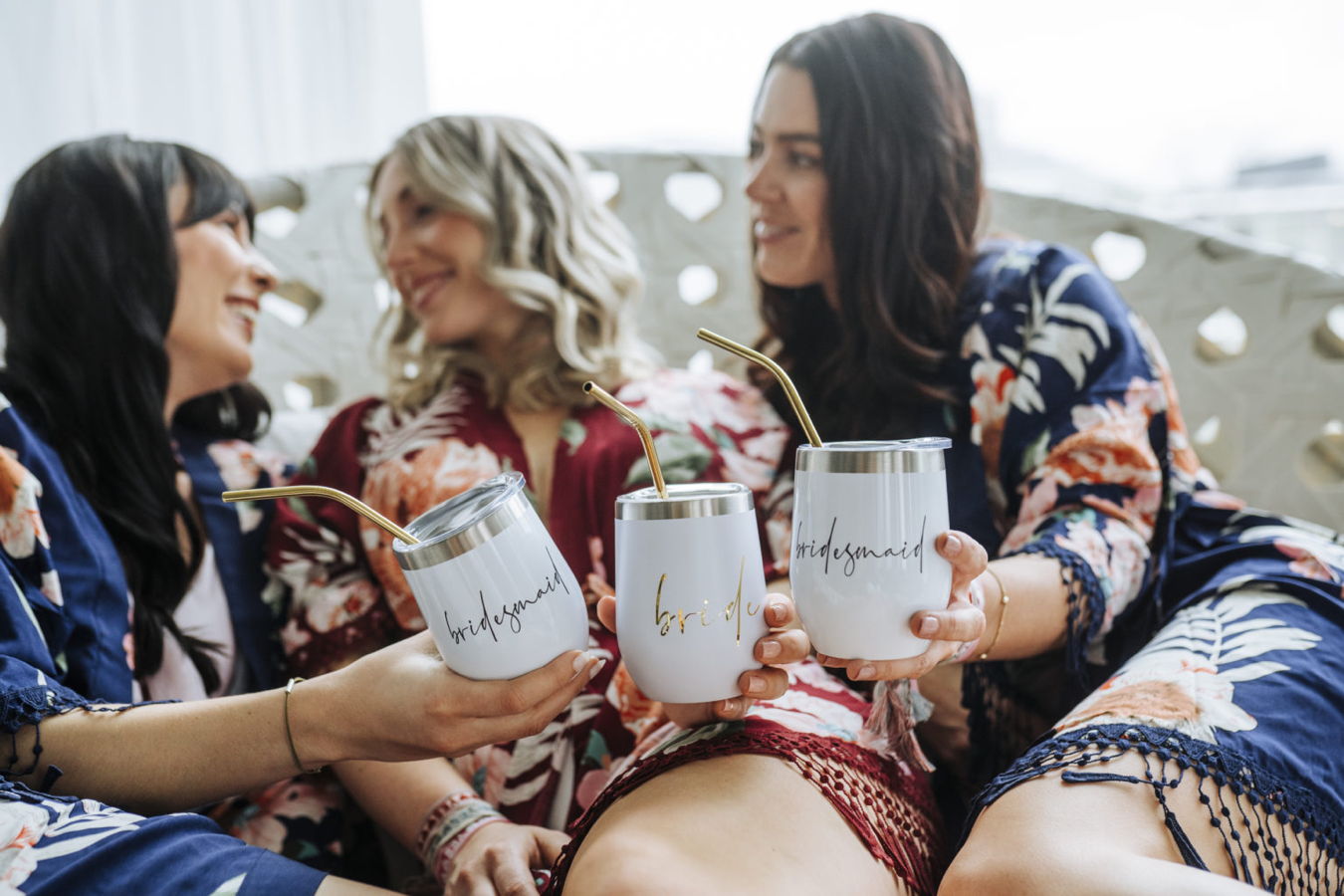 Drei Frauen stoßen mit Bechern an, auf denen „bridesmaid“ und „bride“ steht