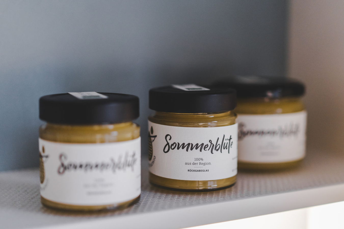 Drei Gläser mit Aufstrich mit der Aufschrift „Sommerblüte“ und schwarzem Deckel