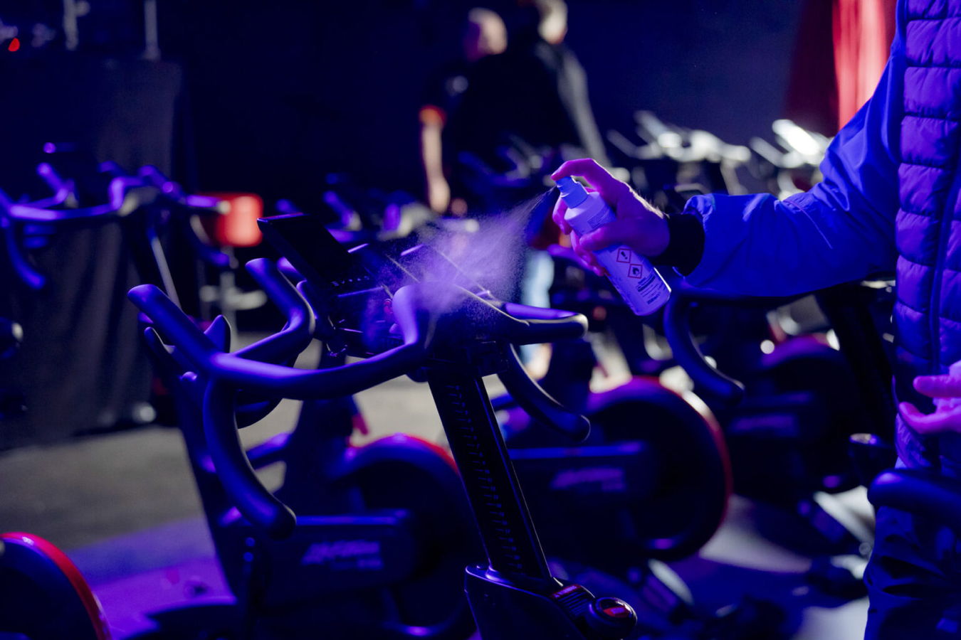 Jemand desinfiziert einen Spinning-Bike-Lenker mit Spray in einem Fitnessstudio