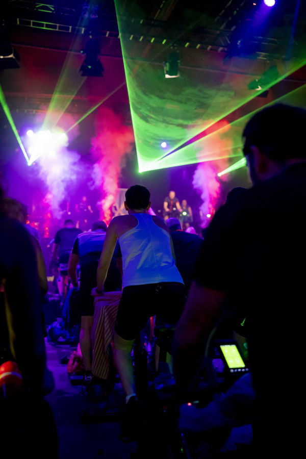 Teilnehmer beim Indoor-Cycling unter bunten Laserlichtern und Bühnennebel