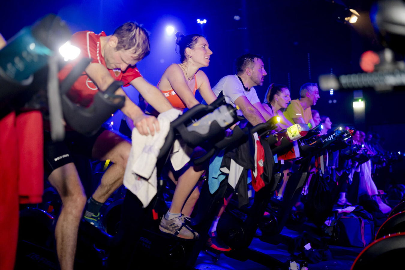 Menschen trainieren auf Indoor-Bikes in einem Fitnesskurs mit blau-violetter Beleuchtung