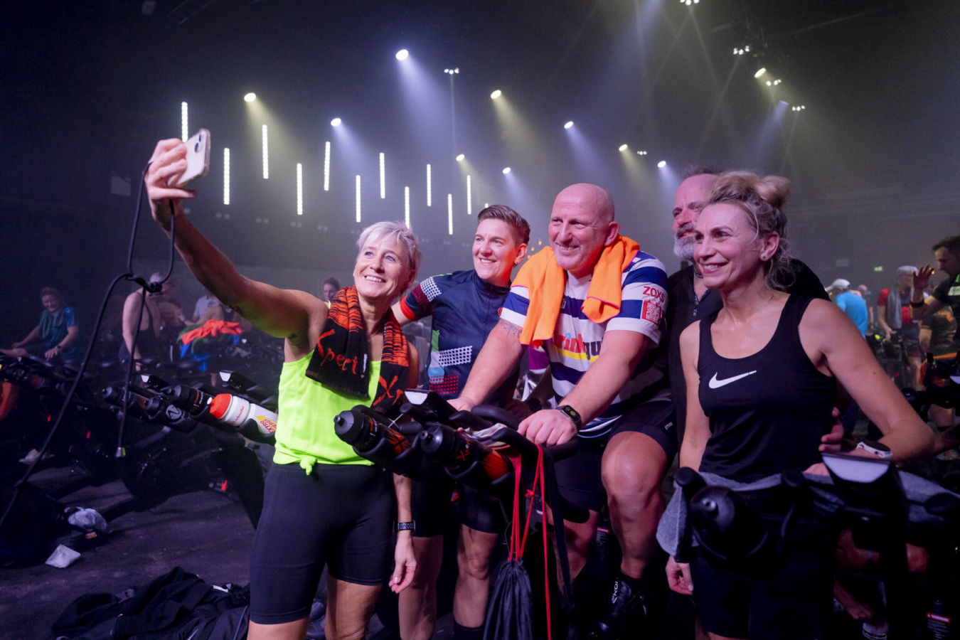 Gruppe von Radfahrern macht ein Selfie auf stationären Fahrrädern in einer beleuchteten Halle
