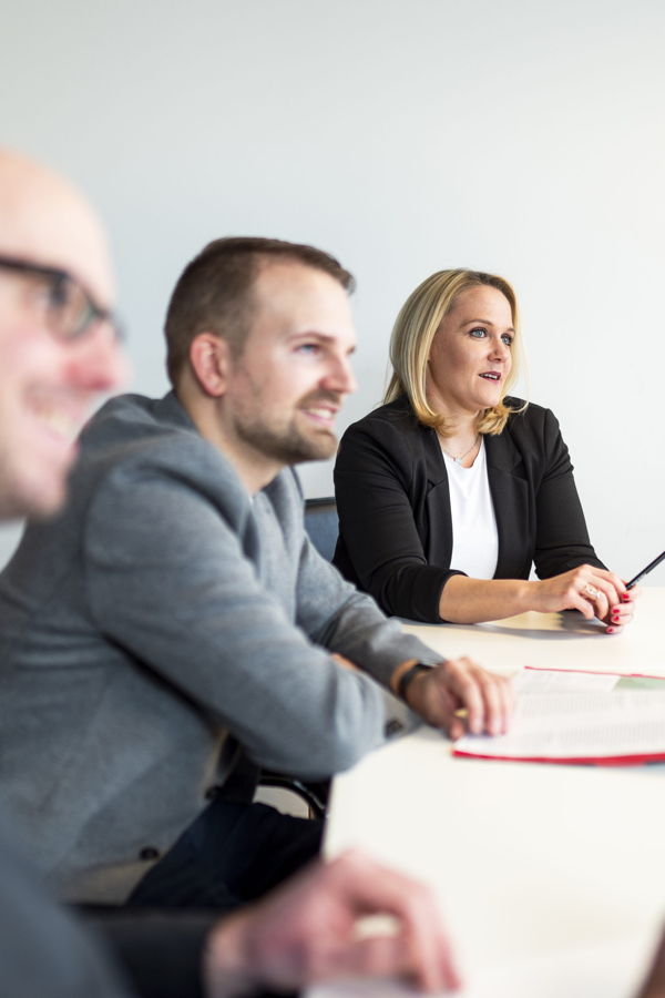 Drei Personen sitzen an einem Tisch in einer Besprechung und hören aufmerksam zu
