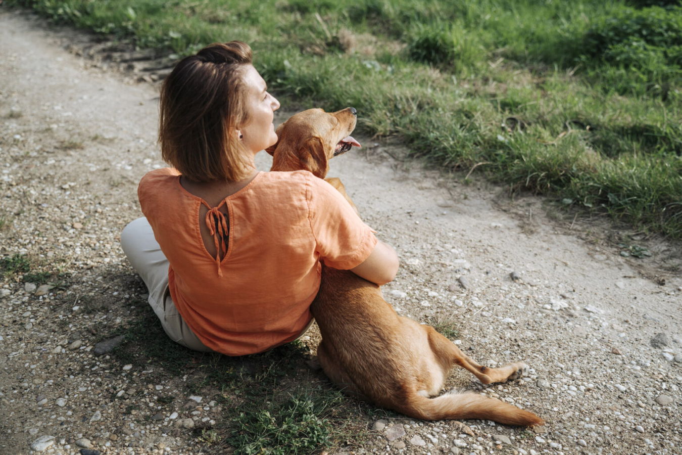 Frau sitzt auf einem Feldweg und hält einen Hund im Arm