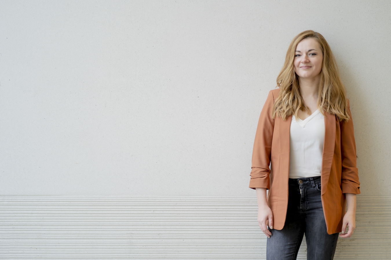 Frau mit orangefarbenem Blazer vor heller Wand