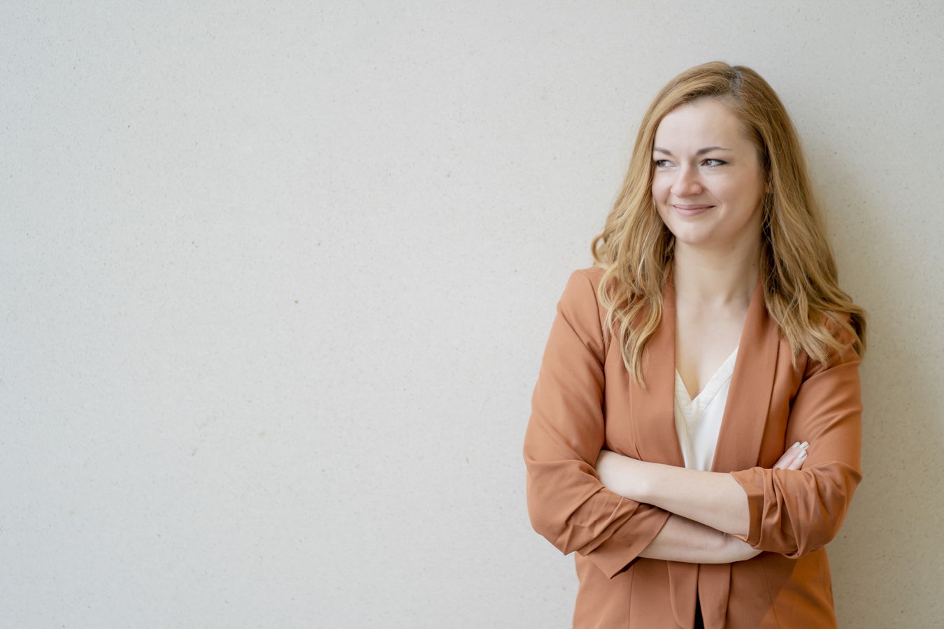 Eine lächelnde Frau mit verschränkten Armen vor einer hellen Wand