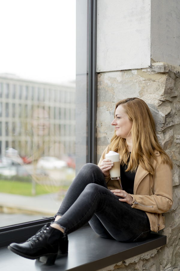 Frau sitzt am Fenster und hält einen Kaffee in der Hand