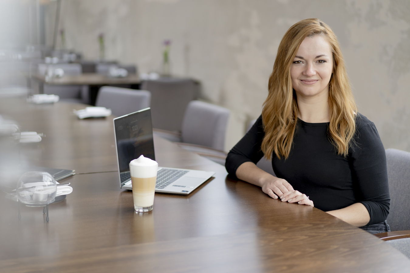 Eine Frau sitzt an einem Konferenztisch neben einem Laptop und einem Latte Macchiato