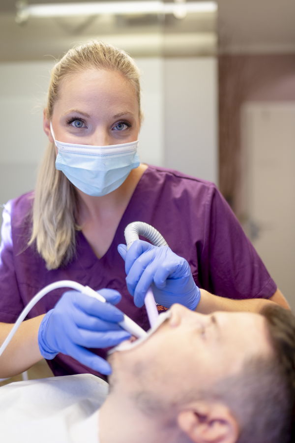 Zahnärztin behandelt einen Patienten mit Mundschutz und Handschuhen