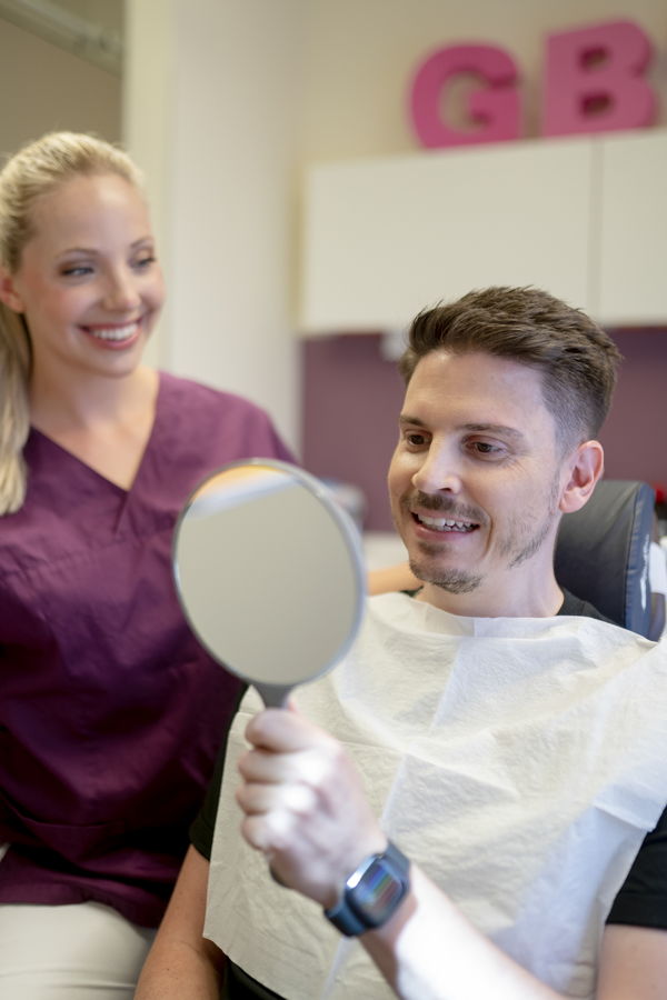 Zahnarztassistentin neben einem Patienten, der einen Handspiegel hält