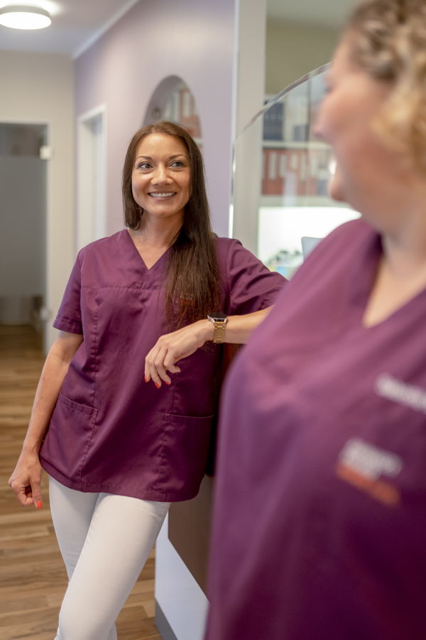 Zwei Frauen in violetten Praxisuniformen stehen in einem Flur und unterhalten sich