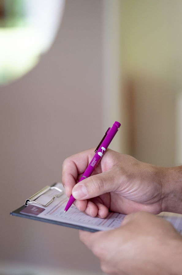 Eine Person füllt mit einem pinken Stift ein Formular auf einem Klemmbrett aus
