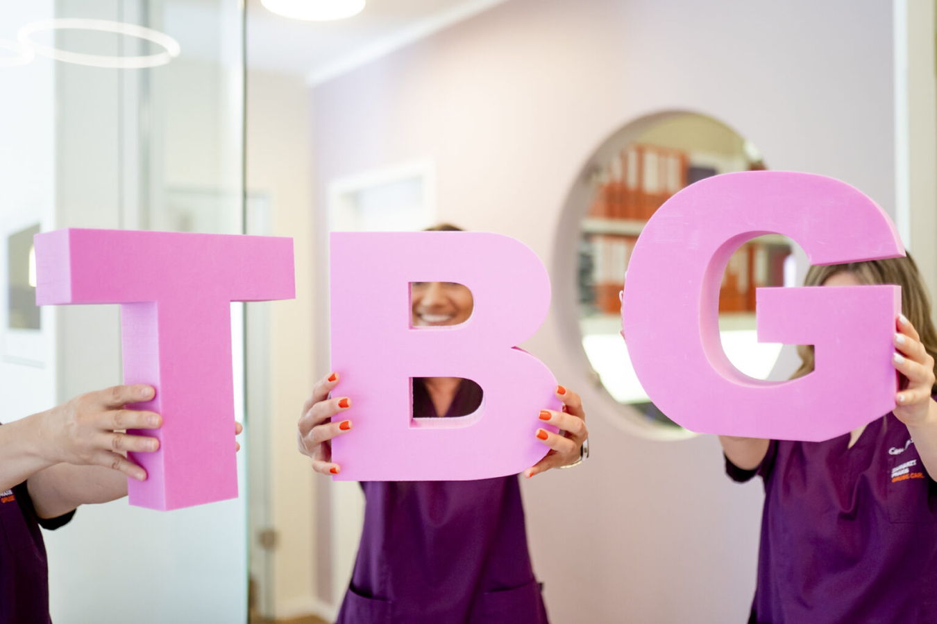 Drei Personen halten große pinke Buchstaben T, B und G vor sich