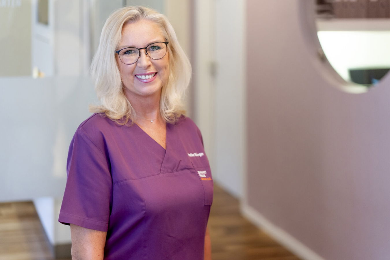 Lächelnde Frau in violetter Berufskleidung mit Brille in einem Innenraum