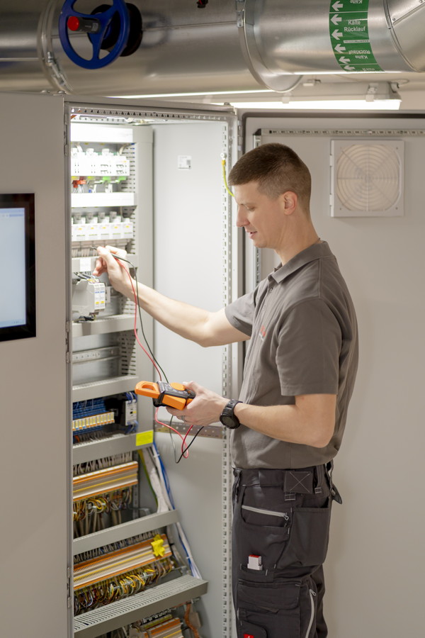Techniker misst an einem geöffneten Schaltschrank mit einem Multimeter