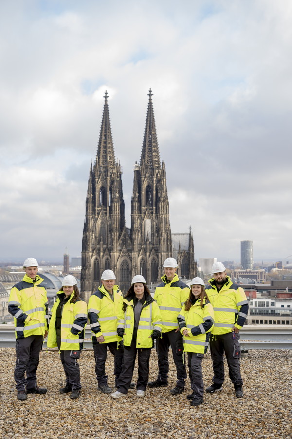 Sechs Bauarbeiter in Warnjacken und Helmen vor dem Kölner Dom