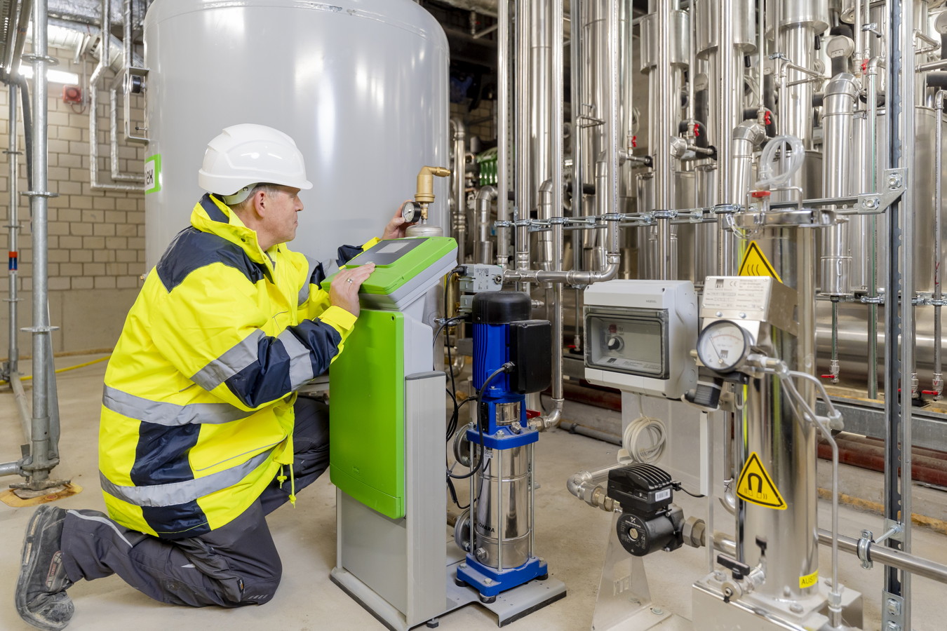 Techniker prüft eine industrielle Rohrleitungsanlage mit Messgeräten in einer Anlagehalle