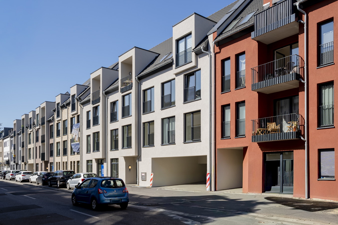 Moderne Wohnhäuser mit Balkonen an einer ruhigen Straße, mehrere geparkte Autos davor