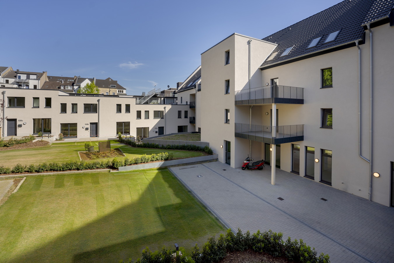 Innenhof einer modernen Wohnanlage mit Rasenflächen, Balkonen und gepflastertem Zugang