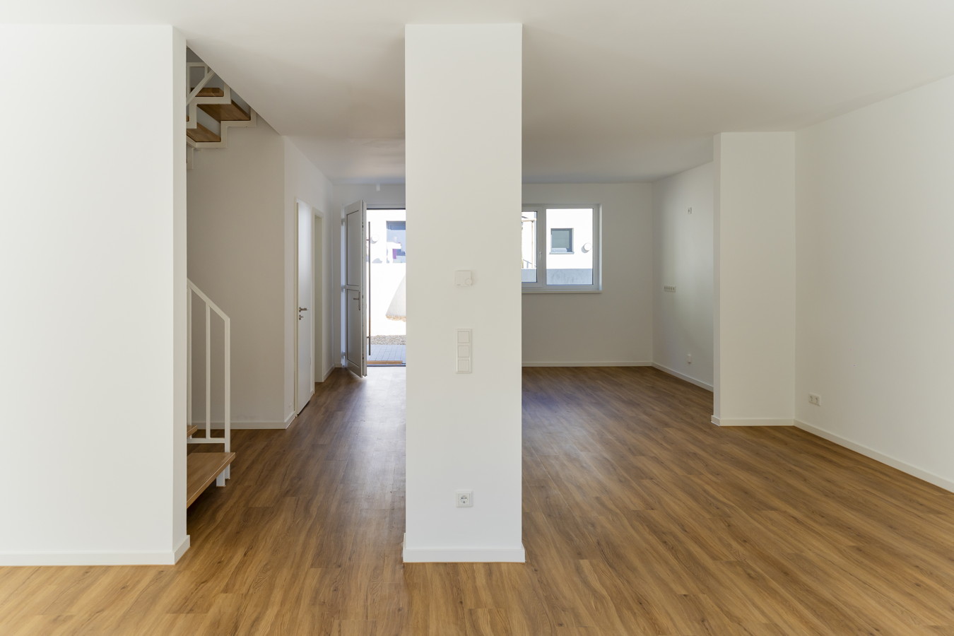 Leerer, modern renovierter Wohnraum mit Holzfußboden, Treppe und offener Tür nach draußen