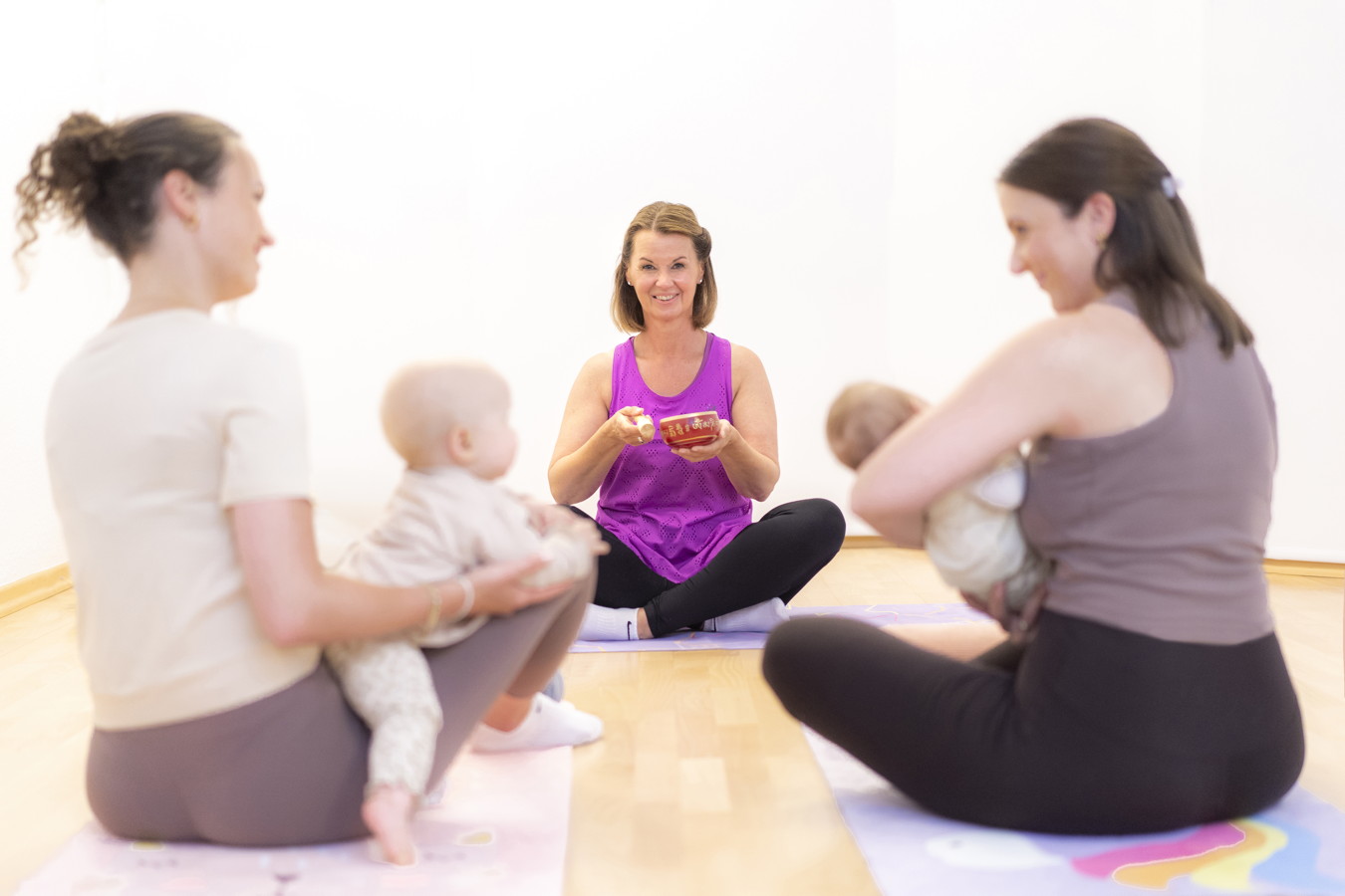 Kursleiterin zeigt Müttern mit Babys eine Übung im Yogakurs