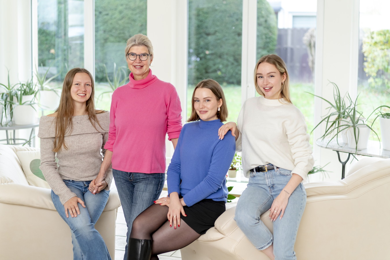 Vier Frauen sitzen und stehen lächelnd in einem hellen Wohnzimmer