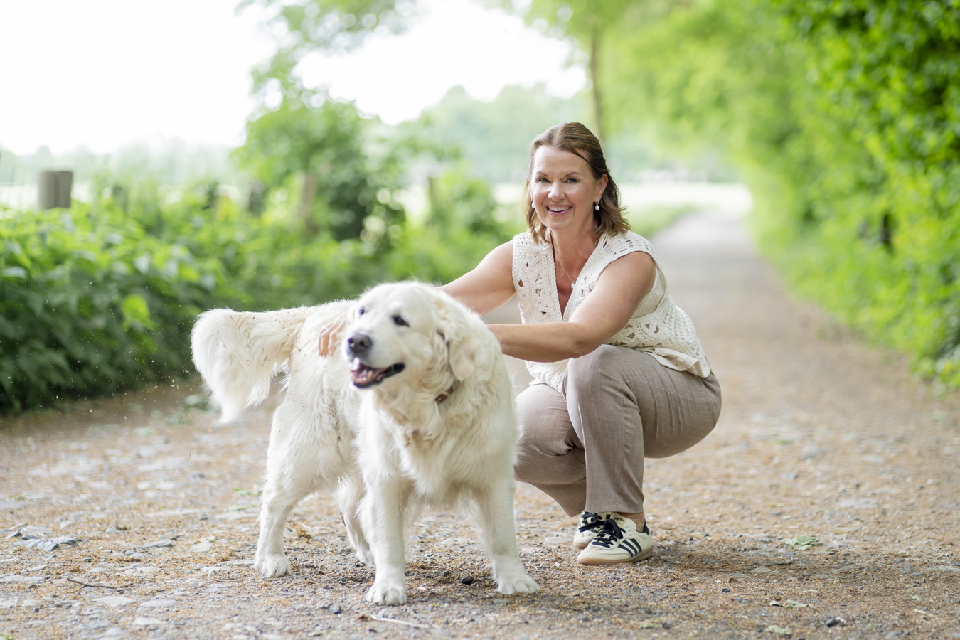 Frau kniet auf einem Waldweg und streichelt einen großen weißen Hund