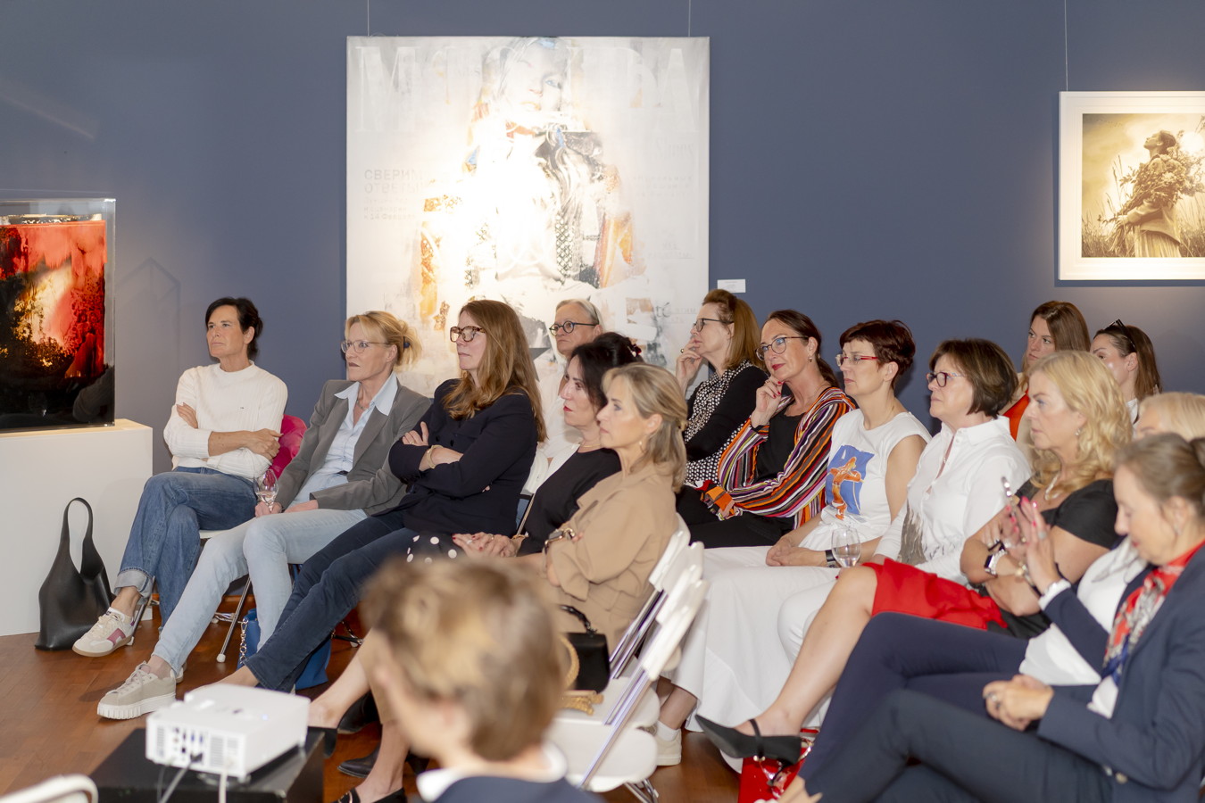 Zuhörerinnen sitzen bei einer Kunstausstellung vor den ausgestellten Bildern
