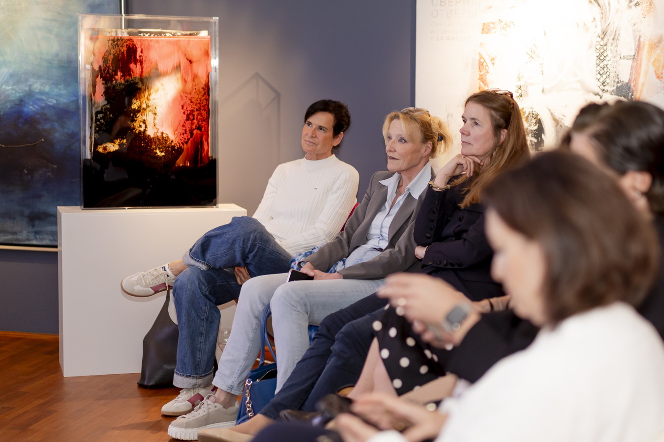 Mehrere Frauen sitzen in einer Galerie und betrachten ein abstraktes Kunstwerk