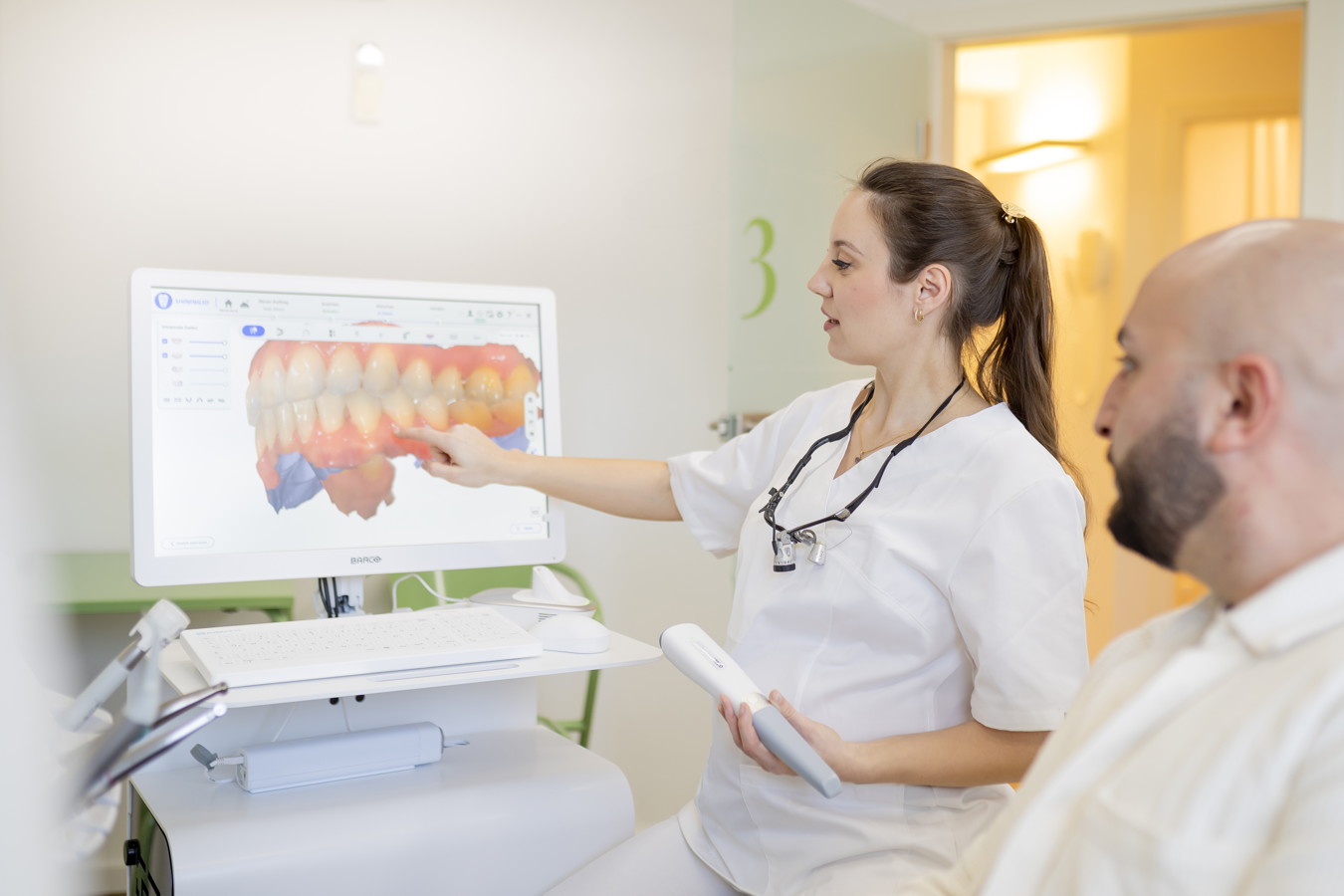 Zahnärztin erklärt einem Patienten eine digitale Zahnaufnahme auf dem Monitor
