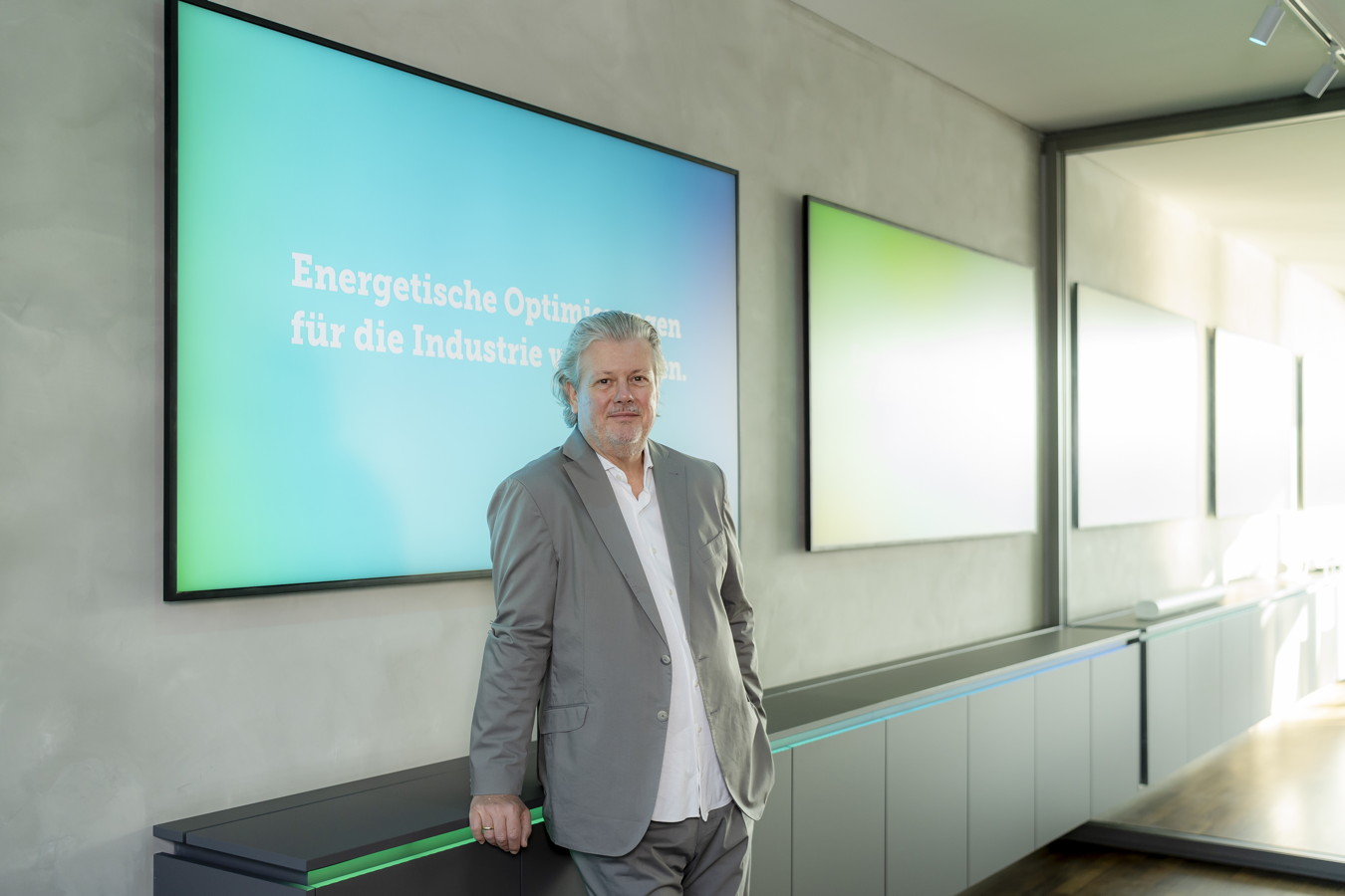 Mann im grauen Anzug steht vor Bildschirmen mit der Aufschrift „Energetische Optimierungen für die Industrie“