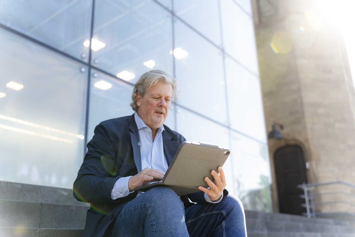 Ein Mann sitzt draußen auf Stufen und arbeitet an einem Tablet