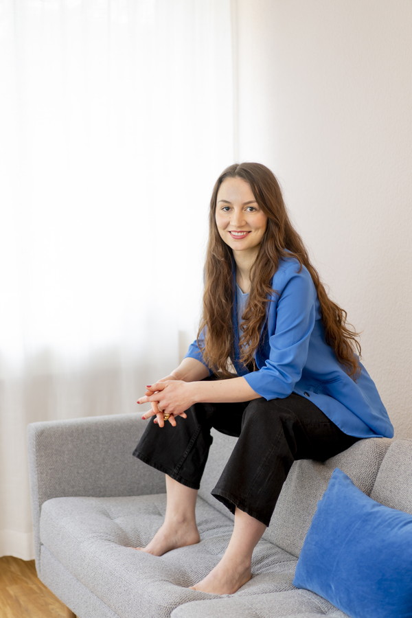 Frau sitzt lächelnd auf einem grauen Sofa in einem hellen Raum