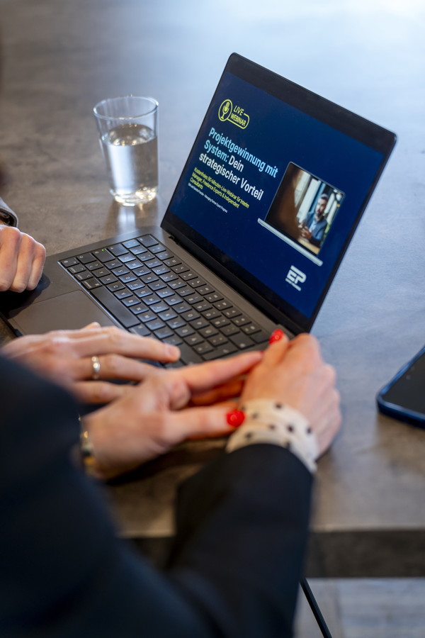 Laptop mit Präsentation zu Projektgewinnung und zwei Personen, die darauf schauen