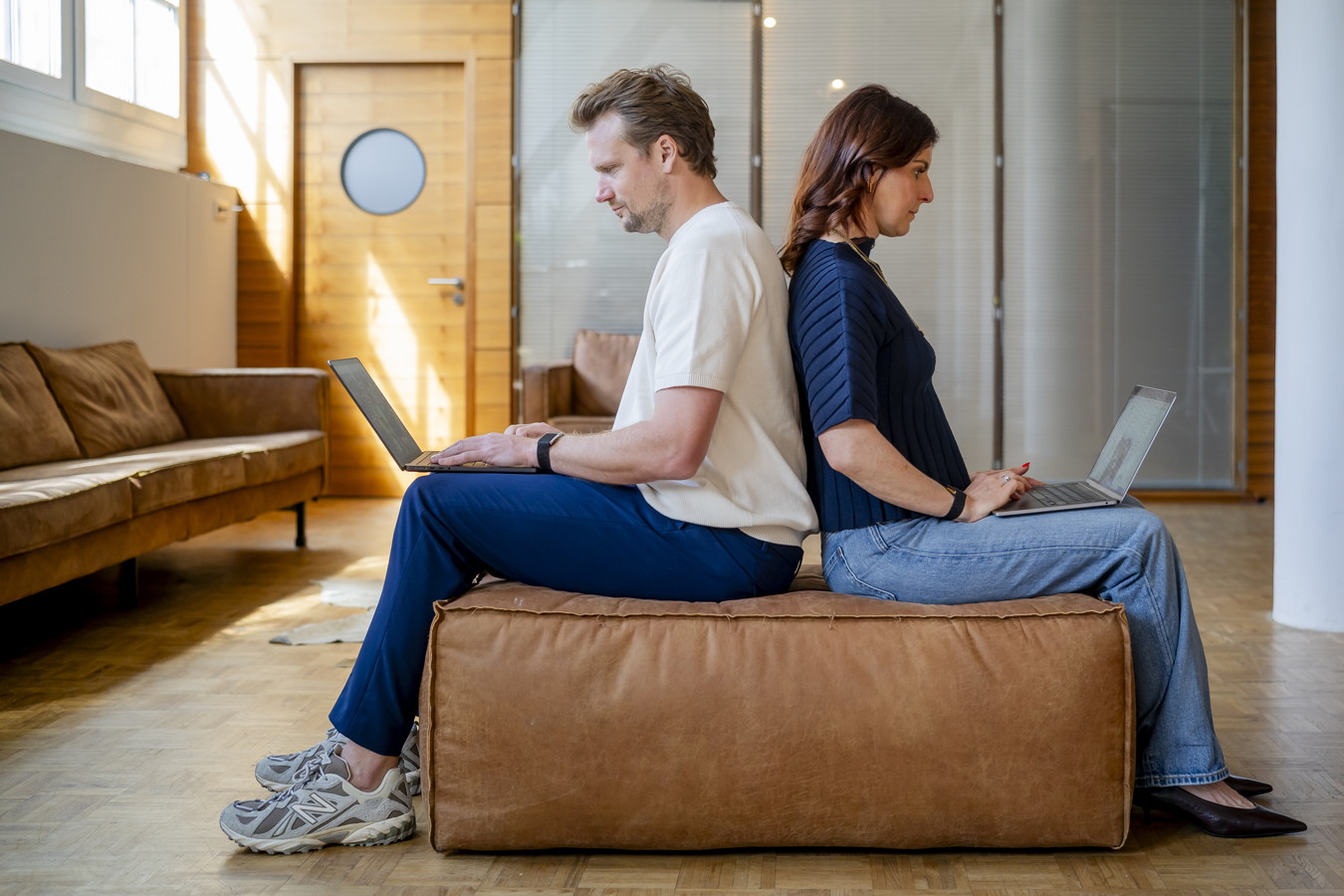 Zwei Personen sitzen Rücken an Rücken auf einer Bank und arbeiten mit Laptops
