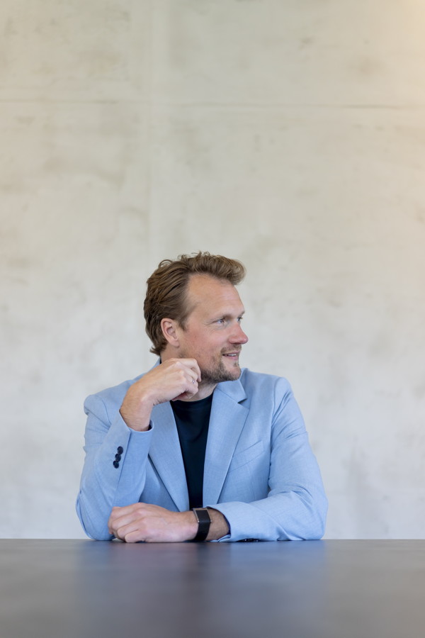 Mann im hellblauen Blazer sitzt an einem Tisch und blickt nach rechts