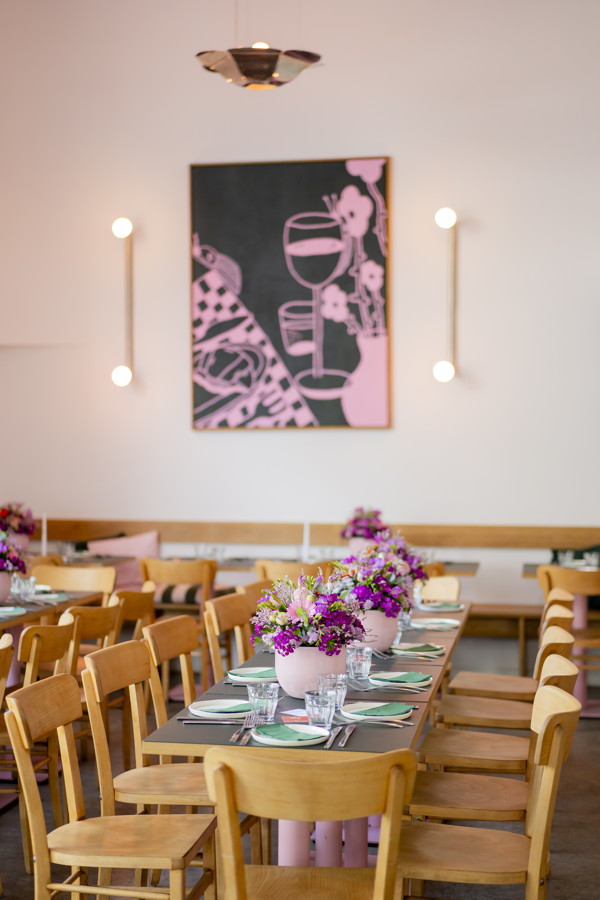 Festlich gedeckter Tisch in einem hellen Raum mit Blumenarrangements und Holzstühlen