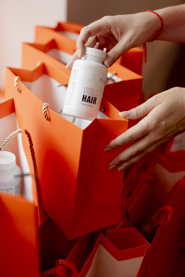Hand legt eine „Full Hair“-Kapsel in eine rote Geschenktüte