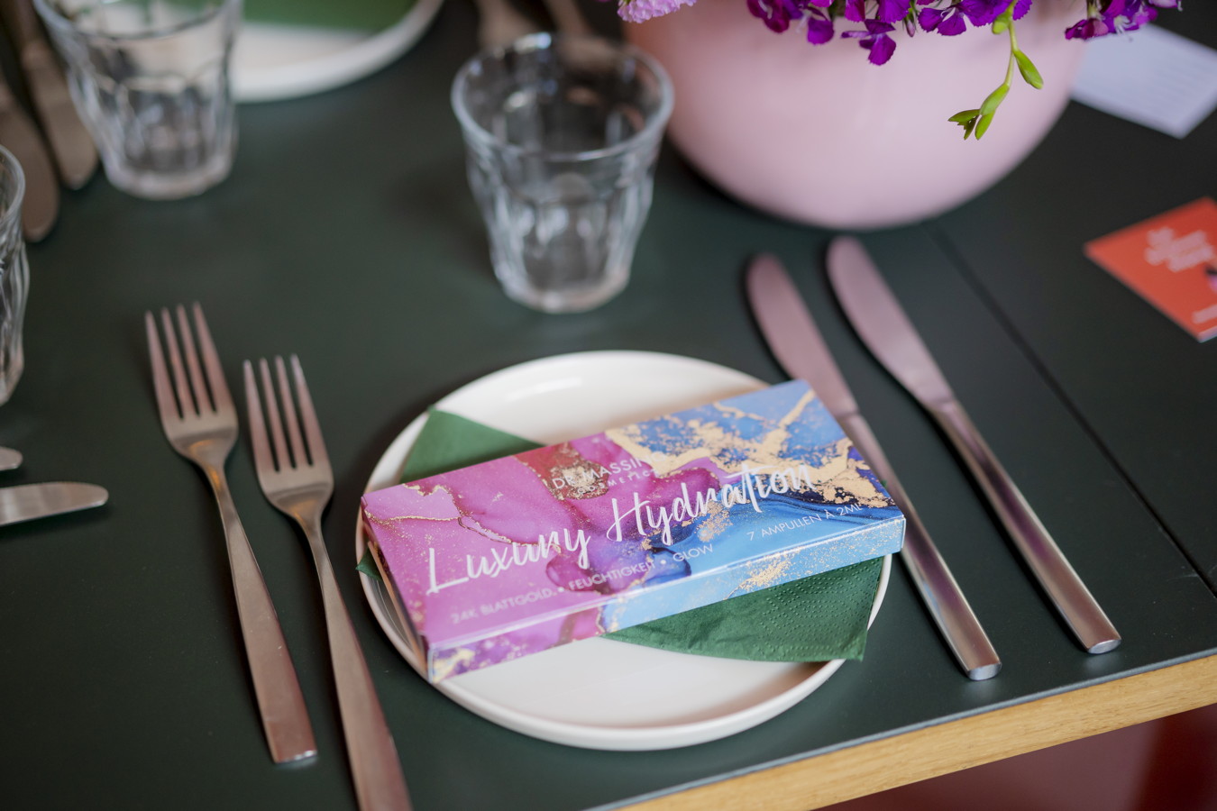 Geschenkbox „Luxury Hydration“ auf einem gedeckten Tisch mit Besteck und Glasen