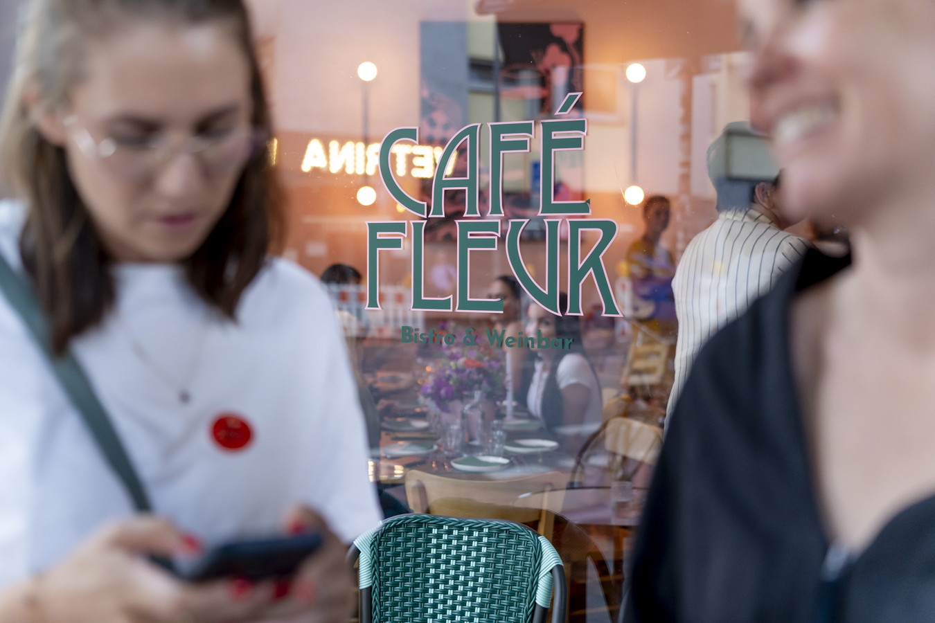 Schaufenster eines Cafés mit der Aufschrift „CAFÉ FLEUR“ und „Bistro & Weinbar“, davor unscharfe Passanten