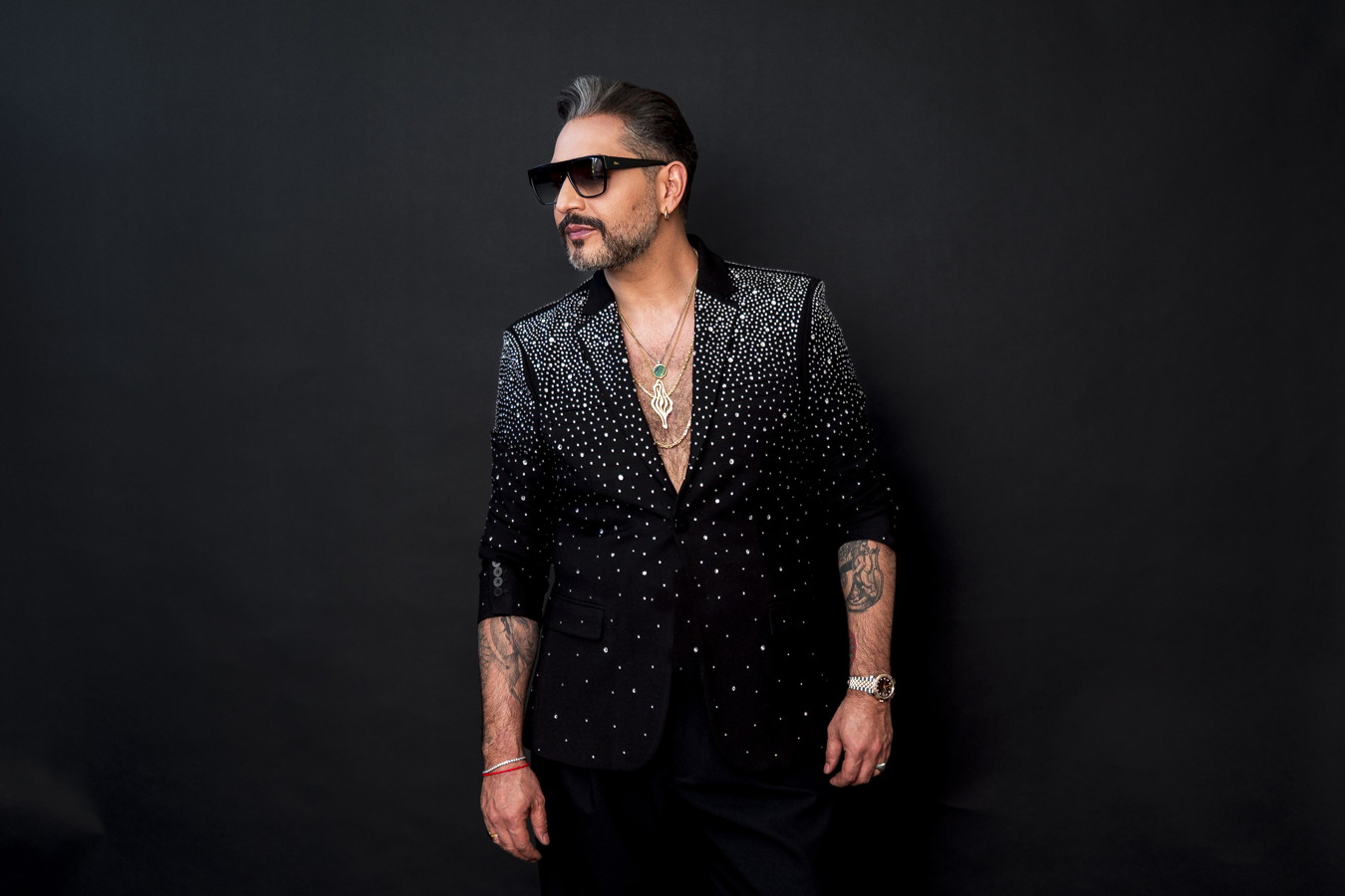 Mann mit Sonnenbrille und glitzerndem schwarzem Jackett vor dunklem Hintergrund