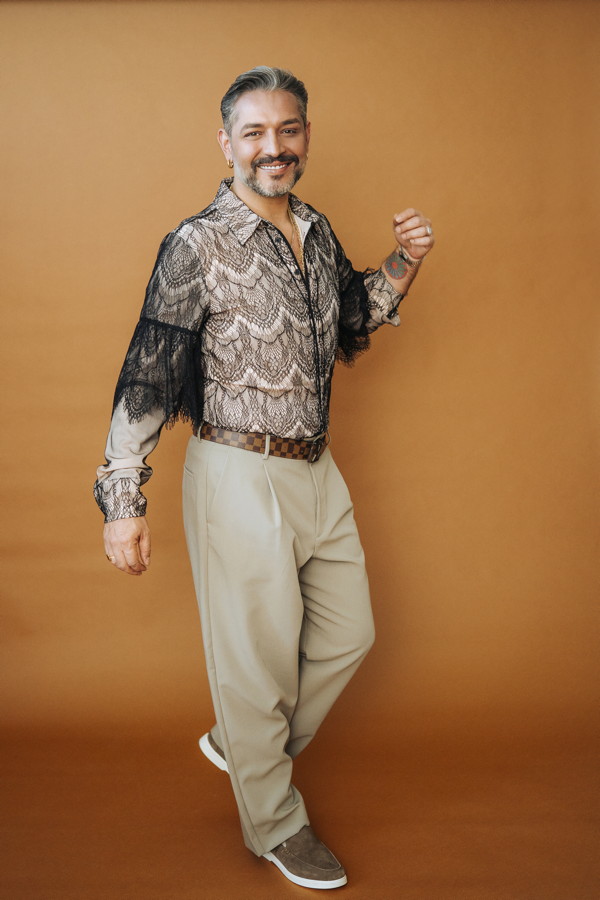 Mann in gemustertem Hemd und beiger Hose vor orangefarbenem Hintergrund