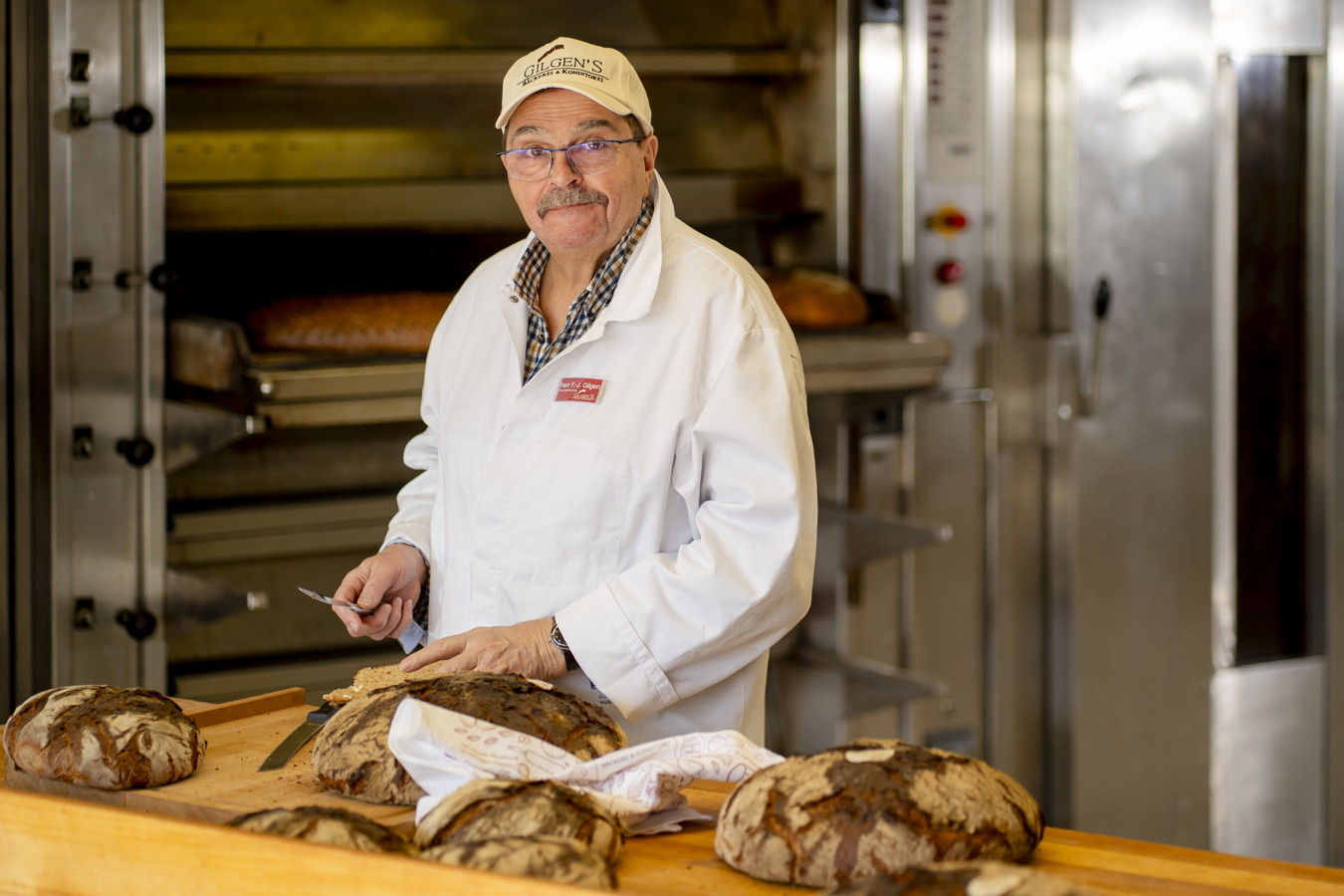Bäcker in weißer Arbeitskleidung schneidet frisches Brot in einer Backstube