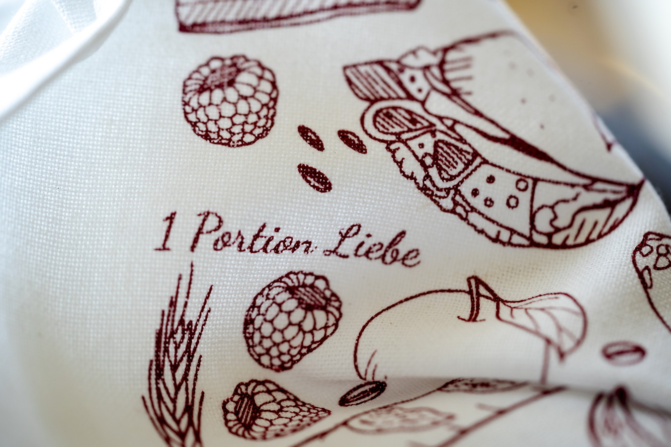 Stoff mit rotem Aufdruck „1 Portion Liebe“ und Illustrationen von Himbeeren und Gebäck