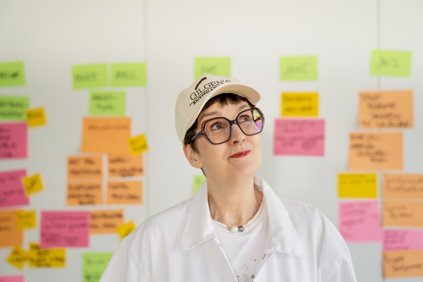 Frau mit Brille und Kappe vor einer Wand mit bunten Haftnotizen