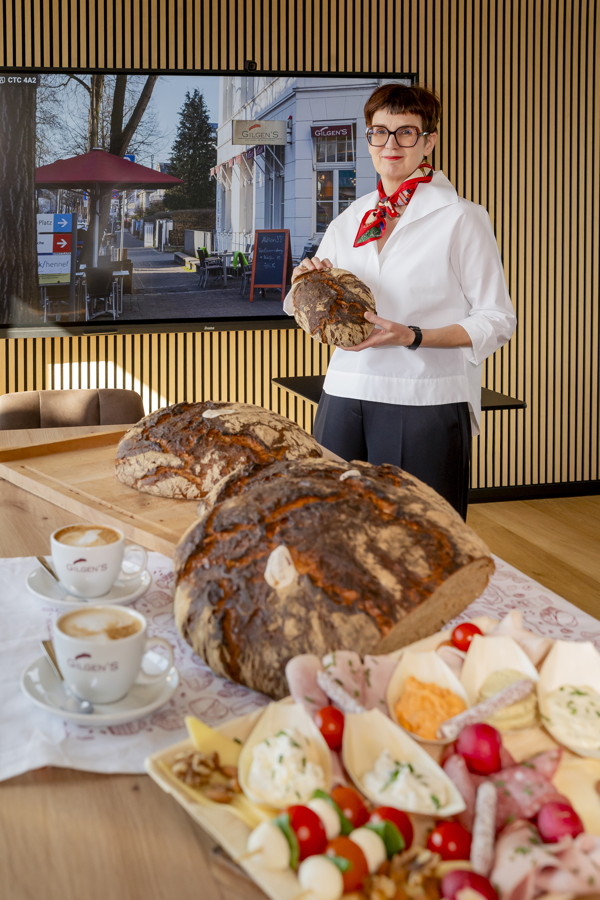 Eine Frau präsentiert Brot und belegte Häppchen auf einem Tisch mit Kaffee und Gebäck