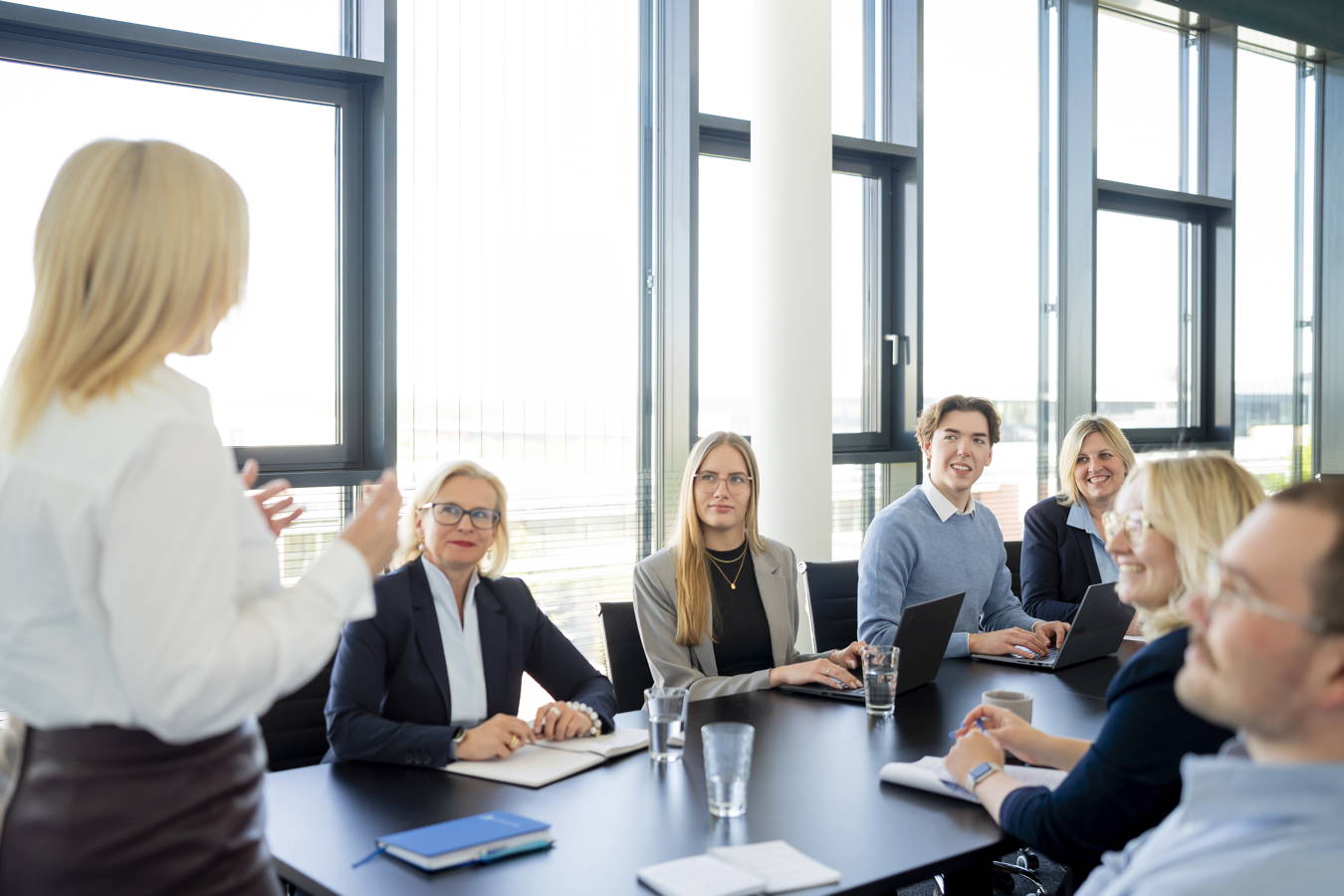 Besprechung in einem Konferenzraum: Eine Frau präsentiert vor mehreren sitzenden Kolleginnen und Kollegen