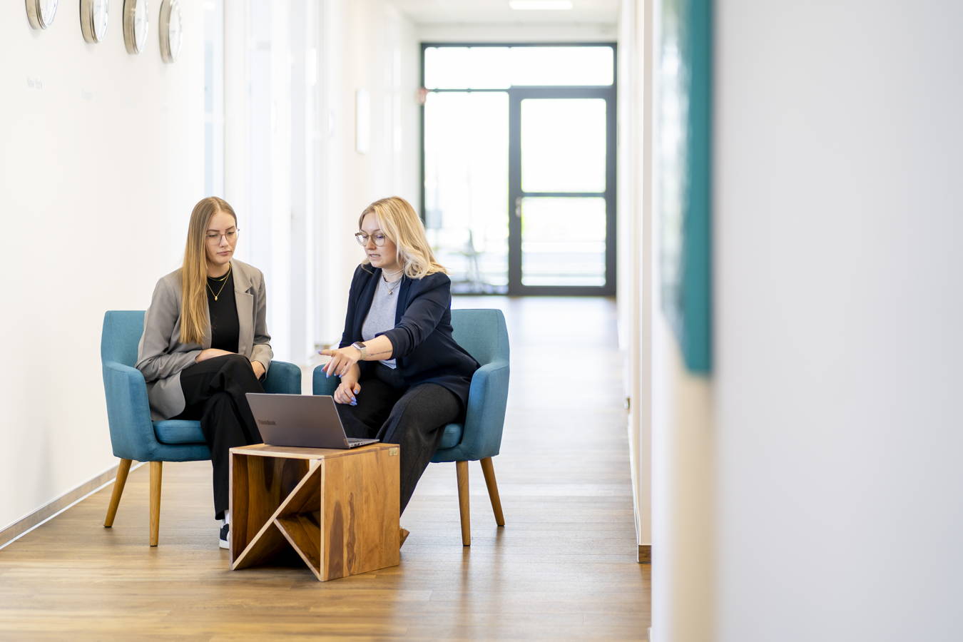 Zwei Frauen besprechen sich in einem hellen Flur vor einem Laptop auf einem Holztisch